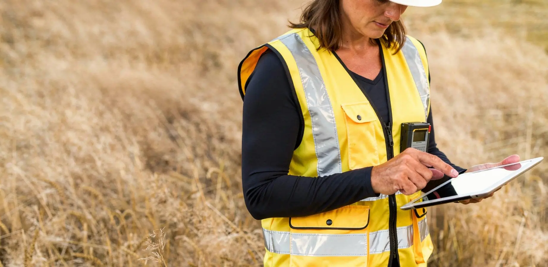 Femme géomètre-expert vérifiant des données sur une tablette numérique dans un champ, lors du contrôle d'un bornage en Savoie