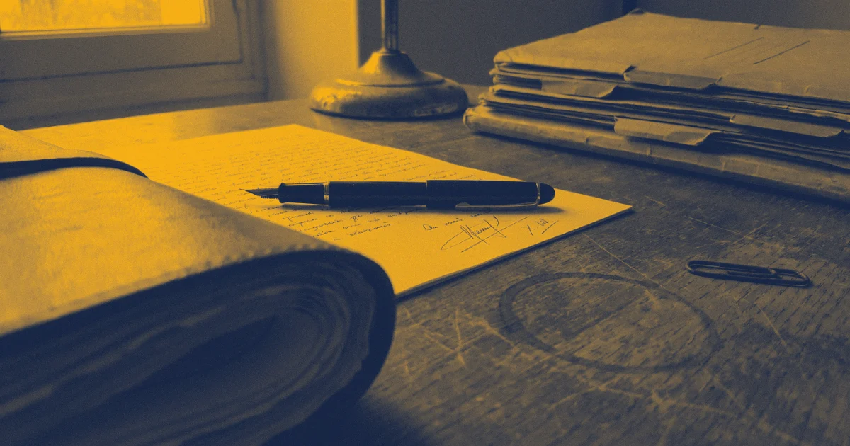 Stylo plume posé sur une lettre manuscrite signée, à côté d'un registre relié, d'une pile de dossiers et d'un trombone, sur une table en bois près d'une fenêtre.